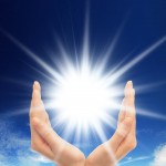 Bright sun between two hands over blue sky showing freedom or solar power concept